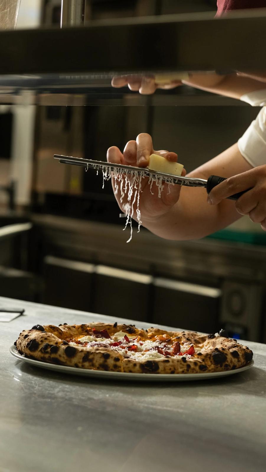 Mutfakta el işçiliği: şef, fırından çıkan pizzaya taze peynir rendeliyor